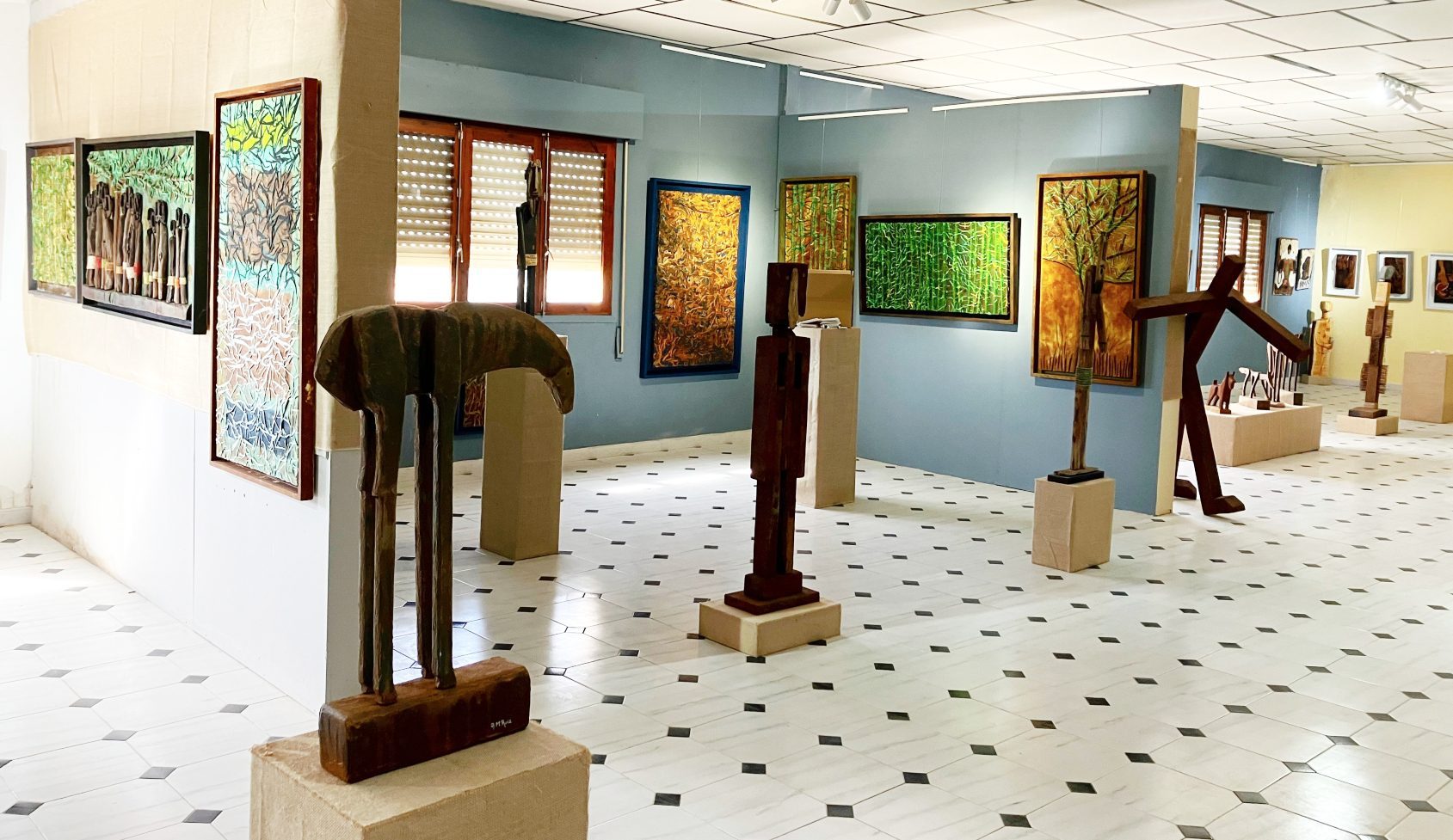 Esculturas altas de madera y óxido sobre peanas, con cuadros al fondo