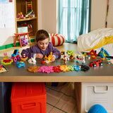 Niño de 5+ años jugando con LEGO Classic 11045 en habitación infantil, seleccionando ladrillos junto a mini-modelos construidos sobre mesa de juego