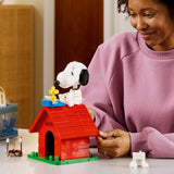 Mujer adulta sonriendo mientras toca el set LEGO Ideas 21368 Snoopy's Doghouse terminado sobre mesa cálida - colección Peanuts para fans adultos 18+