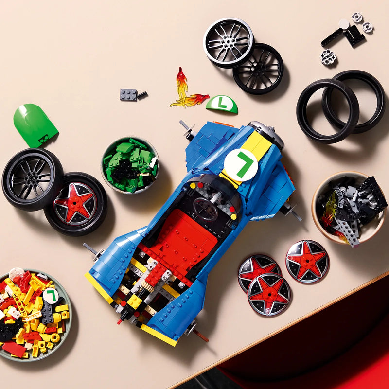 Vista cenital de piezas LEGO Super Mario 72050 Mario Kart en construcción: chasis azul del kart Mach 8 con boweles de ruedas, llamas naranjas, casco verde Luigi y discos estrella roja preparados