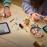 Dos niños construyendo LEGO Harry Potter 76469 Dobby sobre mesa de madera con tabletas LEGO Builder, baúles marrones, bowl con piezas y figura de Dobby a media construcción