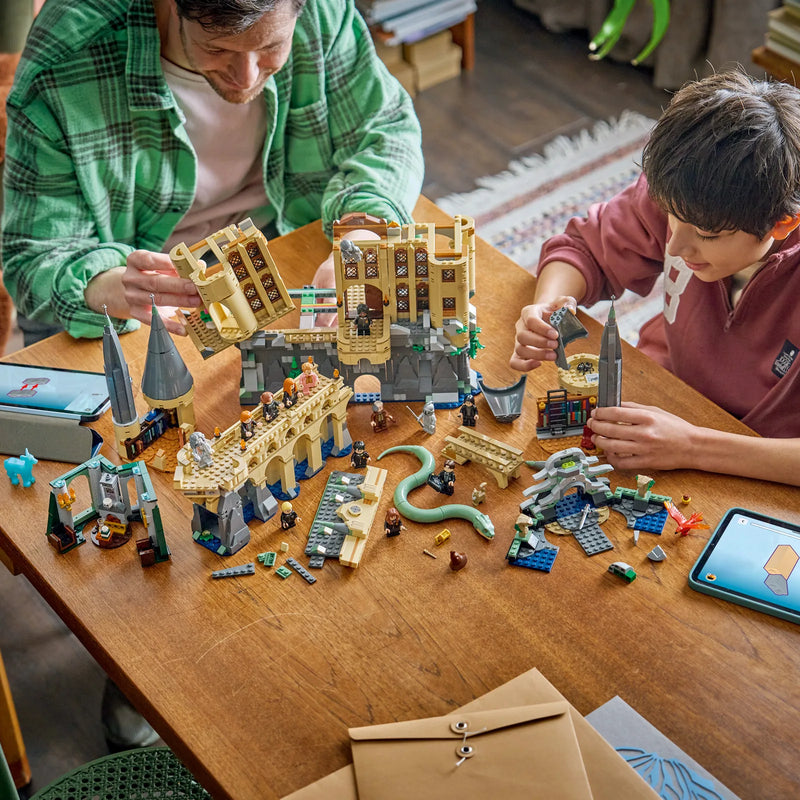 Padre y niño construyendo el set LEGO Harry Potter 76473 Castillo Hogwarts Ala Este sobre mesa de madera con tabletas LEGO Builder y piezas del castillo - sesión Build Together