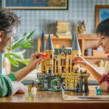 Padre e hijo sonriendo mientras juegan con el set LEGO Harry Potter 76473 Castillo Hogwarts Ala Este montado - 25 Years of Magic en habitación cálida