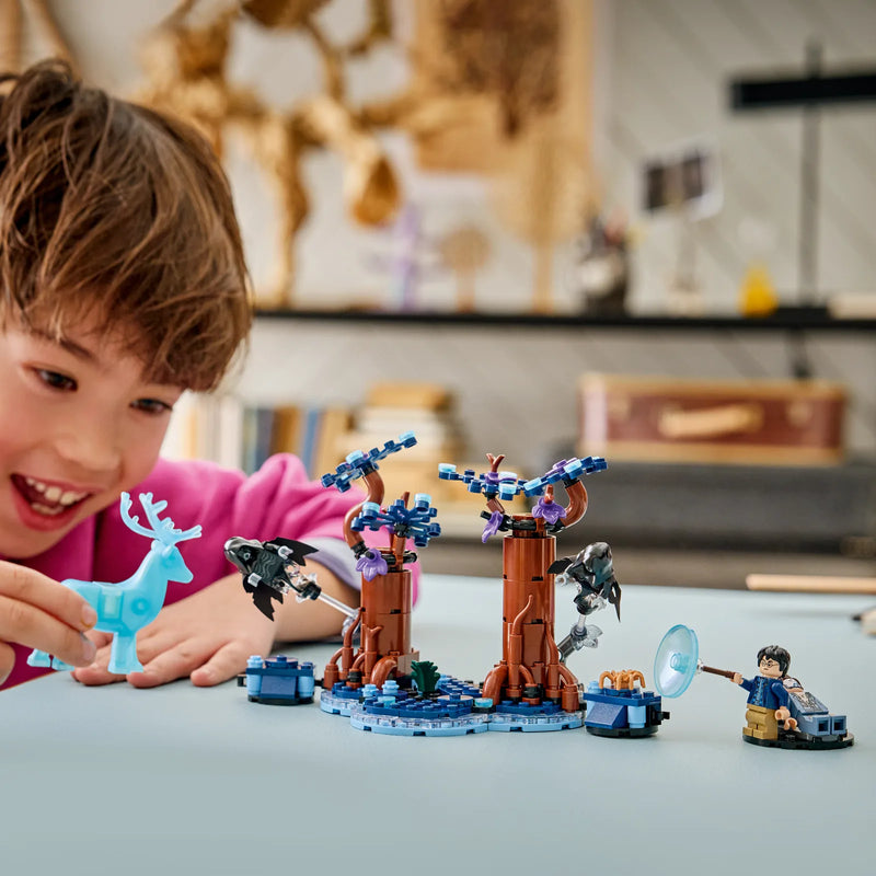 Niño sonriendo mientras juega con el ciervo patronus azul translúcido del set LEGO Harry Potter 76475 Bosque Prohibido Expecto Patronum sobre mesa de habitación infantil