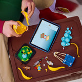 Niño construyendo el set LEGO Fortnite 77080 Supply Drop sobre mesa marrón con tableta LEGO Builder, globo amarillo a medio montar, plataforma verde y minifigs Fortnite
