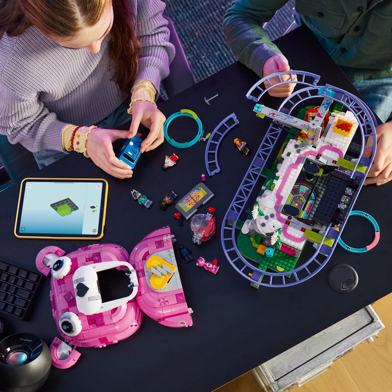 Dos adolescentes construyendo el set LEGO Fortnite 77082 Caverna Descontrol vista cenital: cabeza del oso rosa a un lado y montaña rusa morada a otro con tableta LEGO Builder