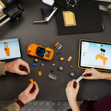 Dos manos adultas construyendo el LEGO Speed Champions 77260 Toyota Supra MK4 Fast & Furious vista cenital - chasis naranja a medio montar, ruedas y tabletas LEGO Builder