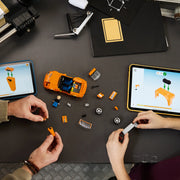 Dos manos adultas construyendo el LEGO Speed Champions 77260 Toyota Supra MK4 Fast & Furious vista cenital - chasis naranja a medio montar, ruedas y tabletas LEGO Builder
