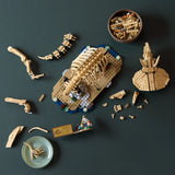 Vista cenital de las piezas LEGO Jurassic World 77985 Triceratops en mesa verde: torso del fósil a media construcción, patas y cola separadas, bowl con ladrillos beige y minifigura paleontólogo