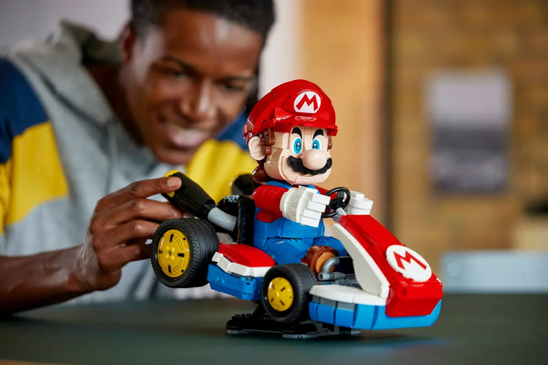 Adulto construyendo LEGO Mario Kart 72037 con figura Mario en kart estándar rojo sobre mesa
