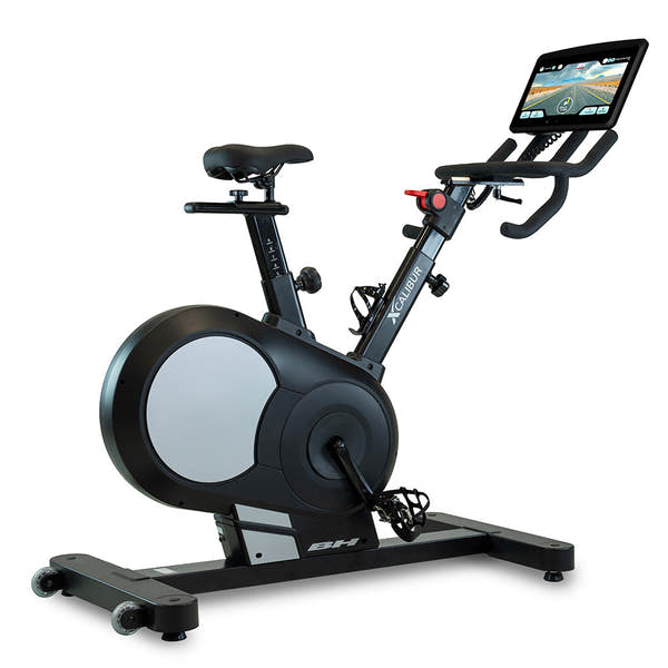 Bicicleta estática BH Xcalibur Silver con pantalla táctil de 16 pulgadas encendida mostrando interfaz multimedia
