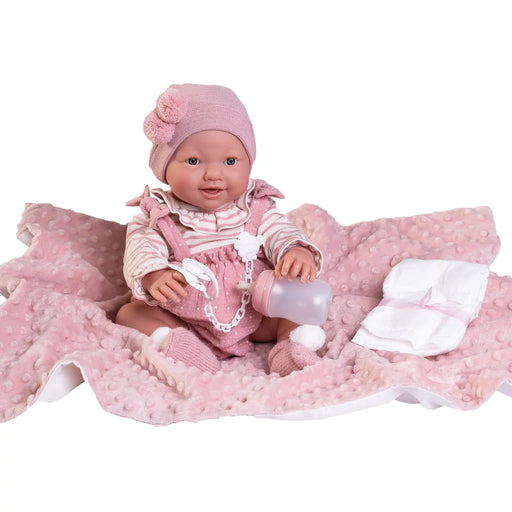 Muñeca Mía hace pipí de Antonio Juan sentada sobre manta rosa con biberón y pañal a la vista
