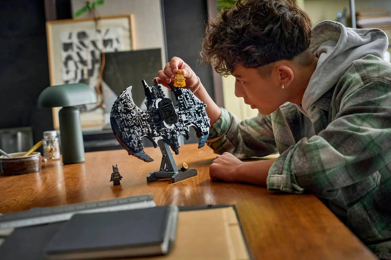 Niño construyendo LEGO Batman 76330 logotipo negro detallado minifigura dorada

