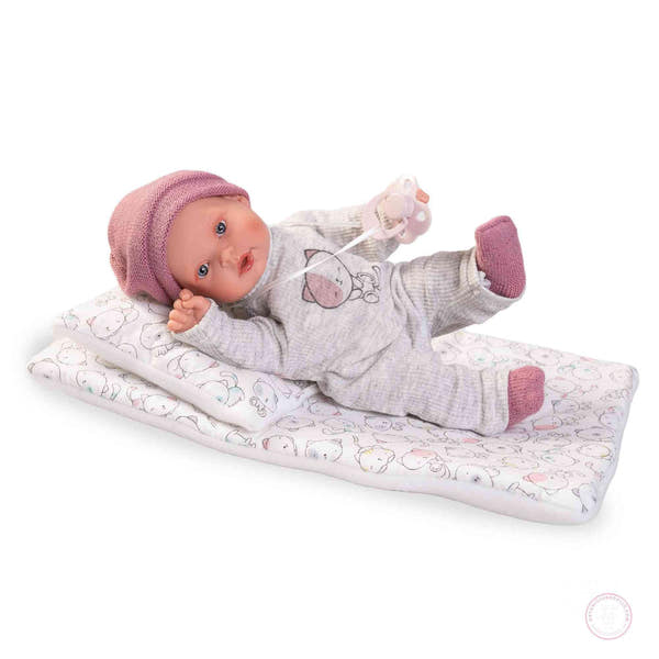 Muñeca Kika Lagrimitas Antonio Juan 11115 sobre su camita con gorrito rosa, pijama gris con gatito y chupete — vista lateral