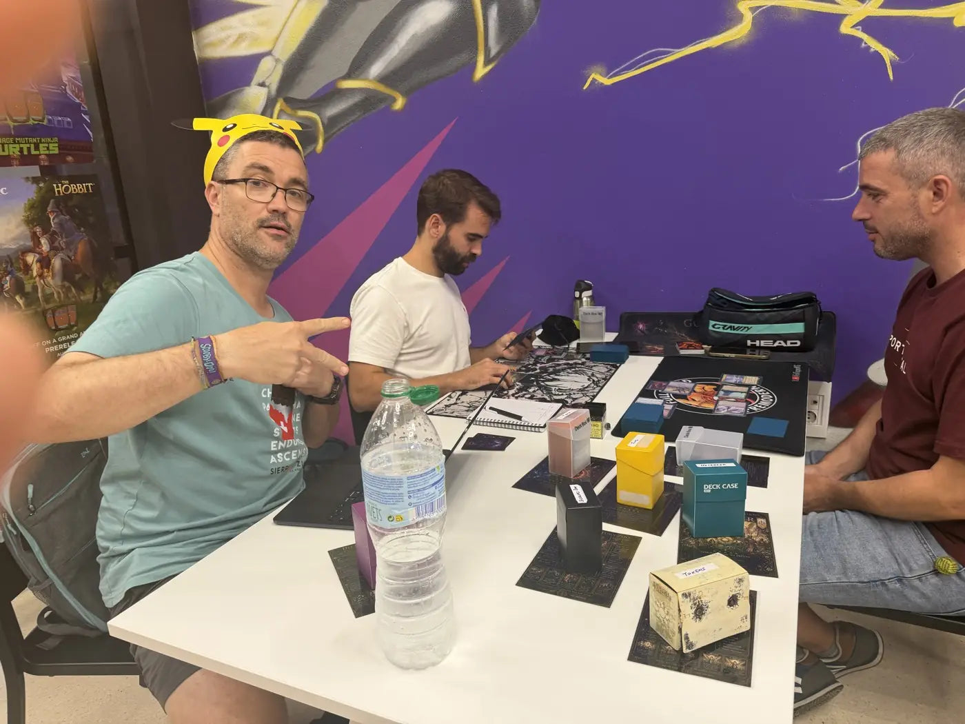 Un jugador con gorra de Pikachu saluda a la cámara mientras su mesa juega