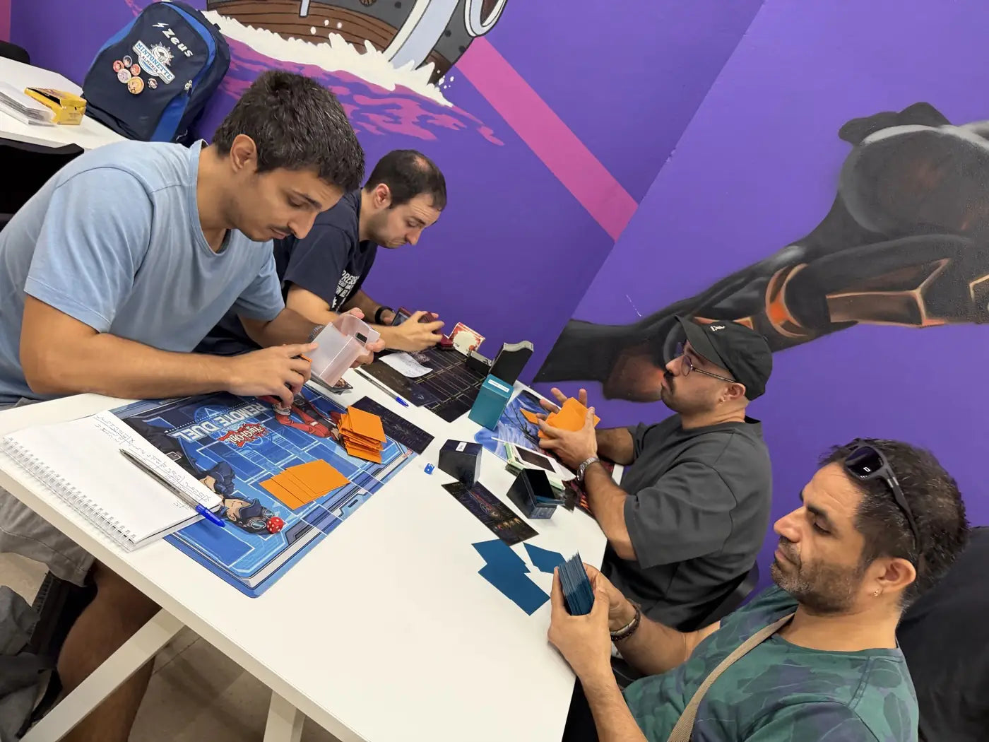 Cuatro jugadores concentrados en dos partidas a la vez, en la mesa junto al mural