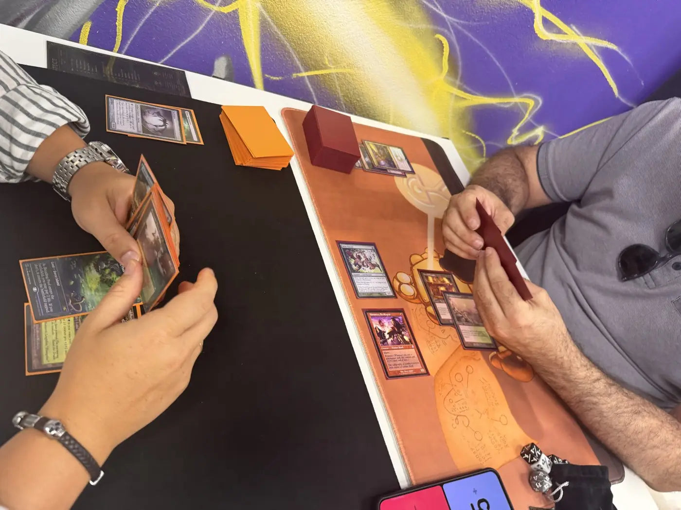 Manos y cartas con fundas naranjas sobre un tapete negro y naranja